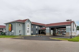 Un hotel con entrada central, estacionamiento y un edificio de techo rojo.