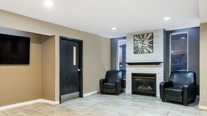 A modern living room with a fireplace, two leather chairs, a flat-screen TV, and a stone accent wall.