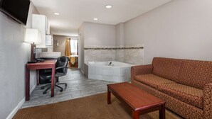 A hotel room with a desk, chair, sofa, and a large bathtub.
