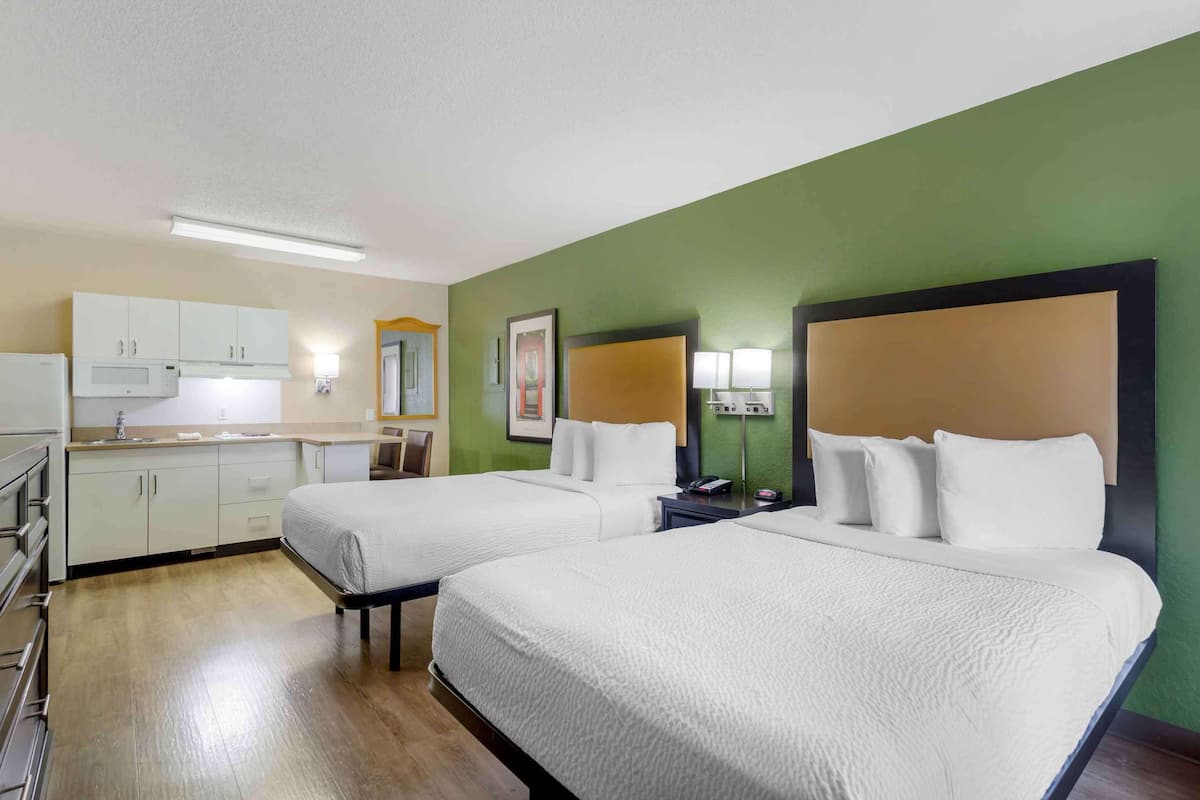 A hotel room with two beds, a kitchenette, and a green accent wall.