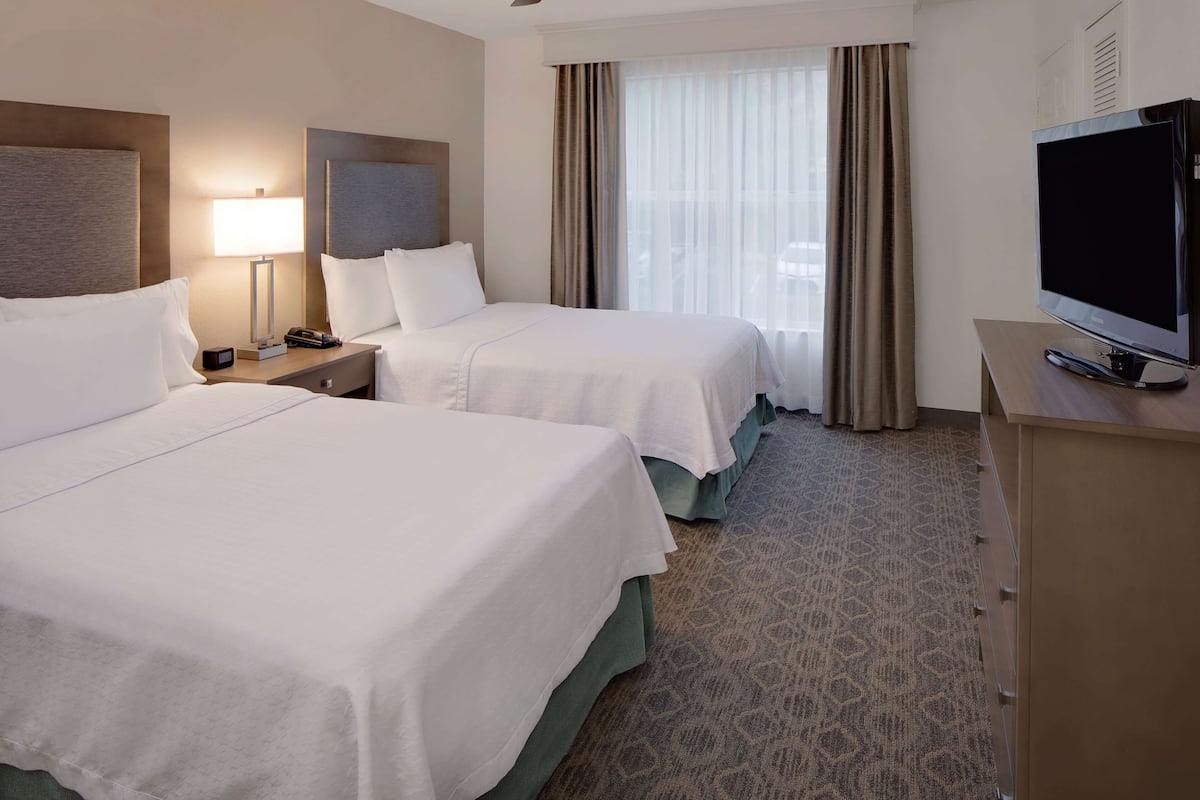 Ein Hotelzimmer mit zwei Betten, einem Fernseher, einem Schreibtisch und einem Fenster mit Vorhängen.