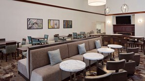 A hotel lobby with a sofa, round tables, and chairs, a television, and artwork on the walls. - Homewood Suites by Hilton Nashville-Brentwood (Brentwood)