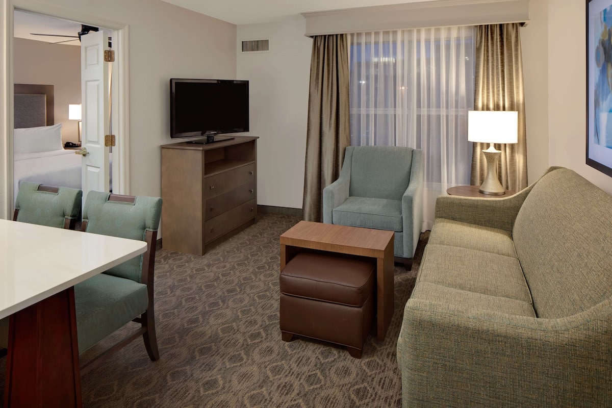 Ein Hotelzimmer mit Bett, Fernseher, Sofa, Sessel, kleinem Tisch und Lampe.