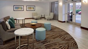 A hotel lobby with a sofa, two armchairs, a coffee table, and a small table with a bowl. There are two framed pictures on the wall, a patterned carpet, and an exit door with a view of the outside. - Homewood Suites by Hilton Nashville-Brentwood (Brentwood)