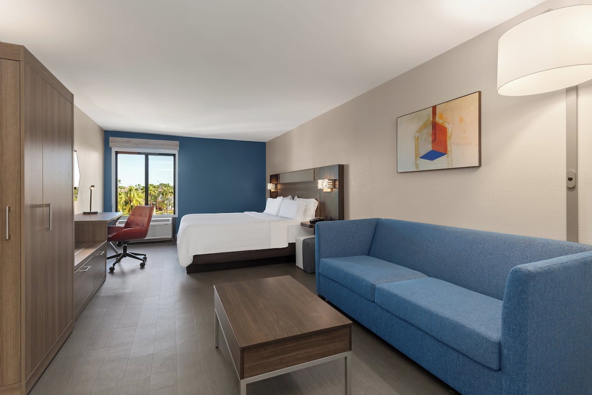 Una habitación de hotel moderna con una cama, un sofá azul, un escritorio y un ventanal grande.