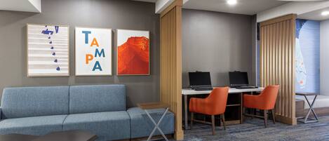 Una habitación de hotel con un sofá azul, un escritorio y dos sillas, y obras de arte en la pared.