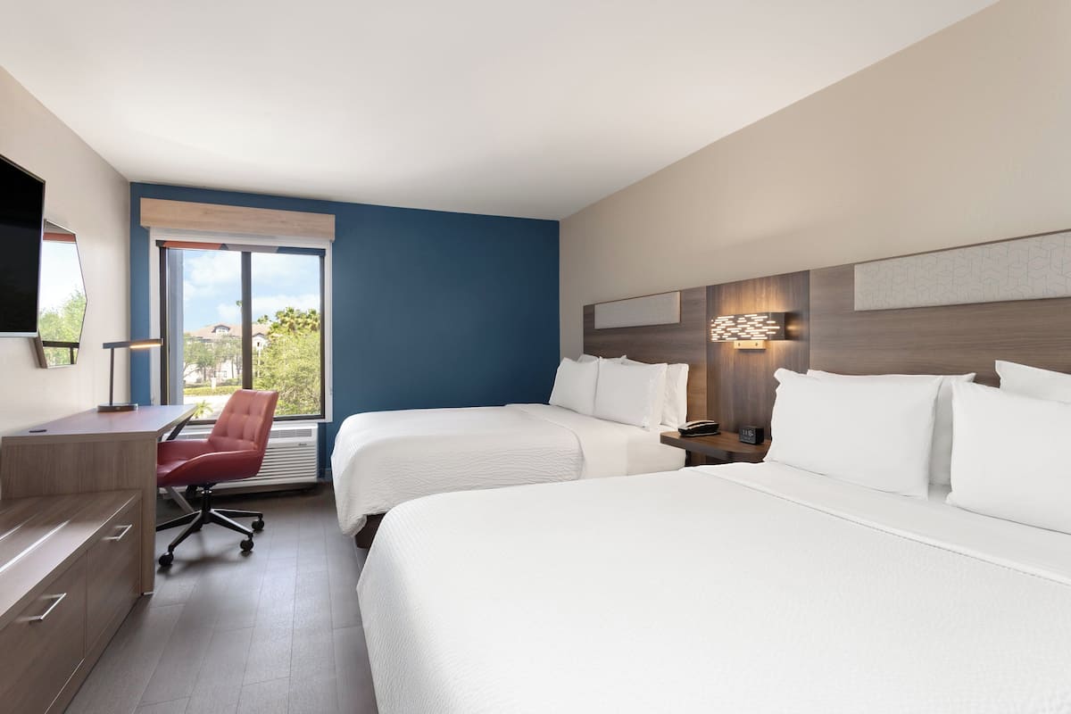 Habitación de hotel con dos camas, un escritorio, una silla y un ventanal grande.