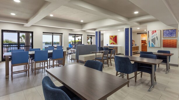 A spacious indoor area with multiple tables and chairs, large windows, and artwork on the walls. - Holiday Inn Express Hotel & Suites Tampa-Rocky Point Island by IHG (Tampa)