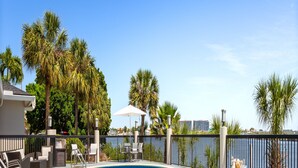 A pool area with lounge chairs and umbrellas, surrounded by palm trees and a view of the city skyline. - Holiday Inn Express Hotel & Suites Tampa-Rocky Point Island by IHG (Tampa)