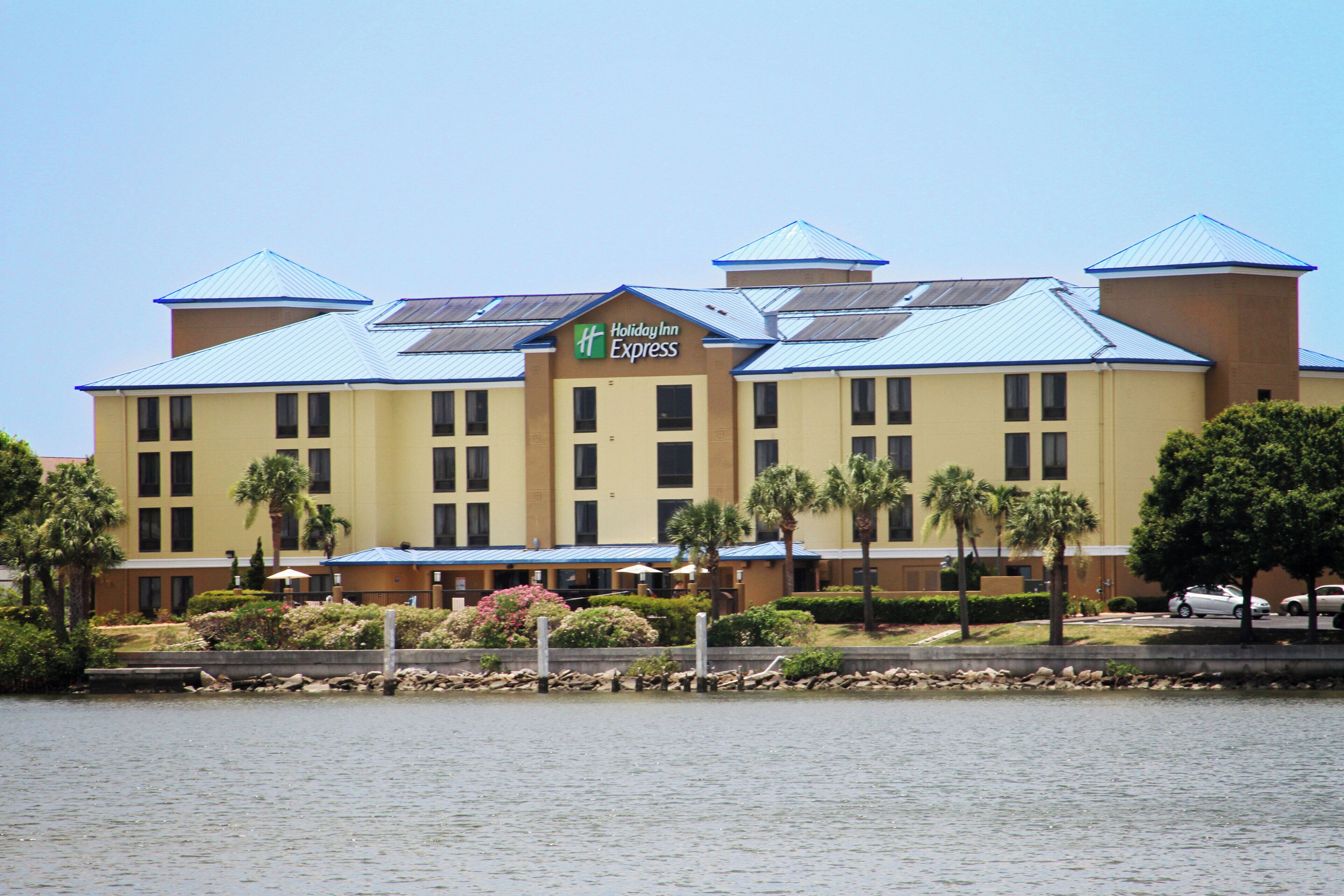 A Holiday Inn Express hotel with a blue roof, multiple windows, and a landscaped front with palm trees.