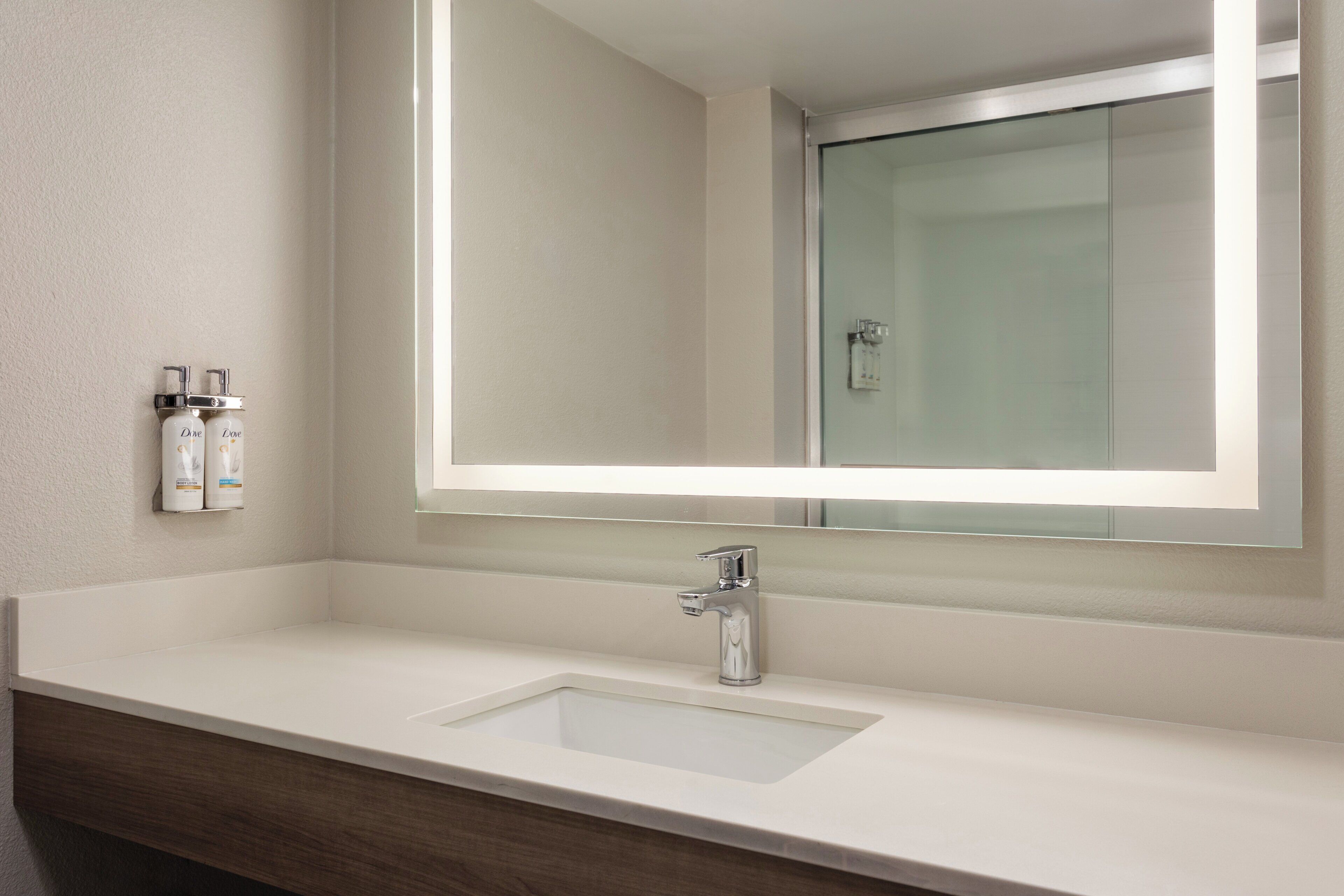 A bathroom with a white sink, a mirror, and two Dove body lotion dispensers.