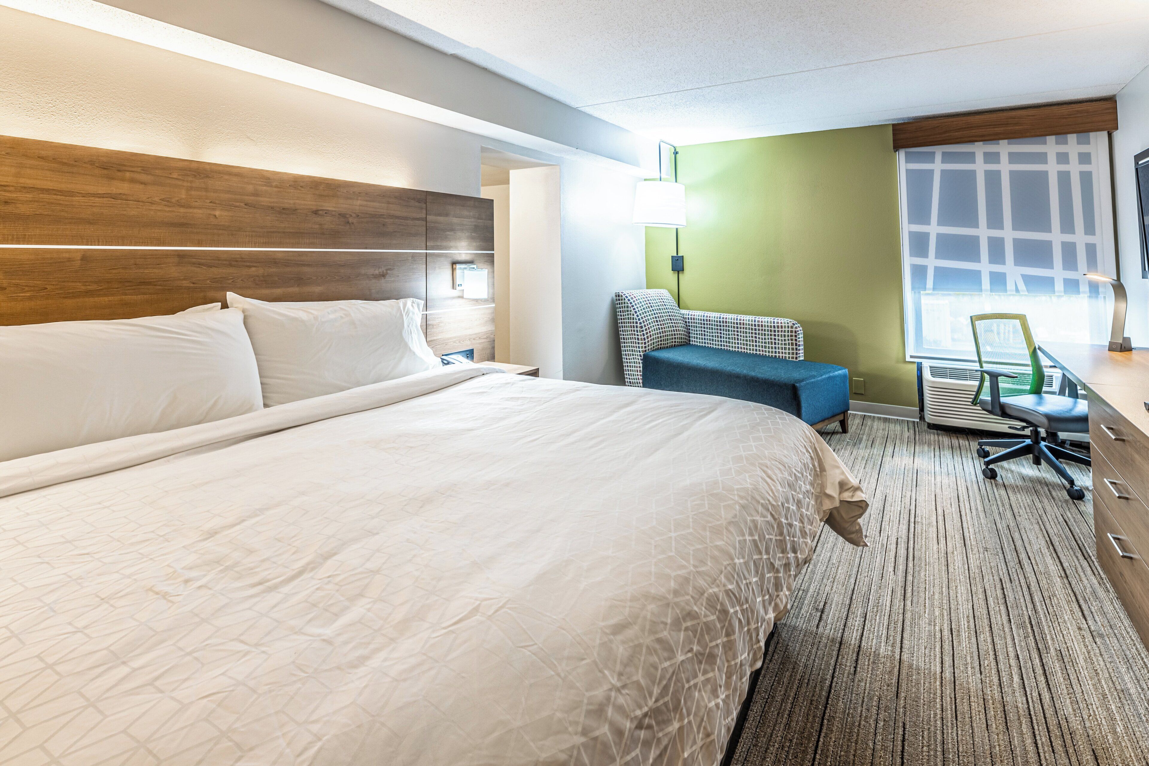 A hotel room with a large bed, a desk with a chair, a lamp, and a window.