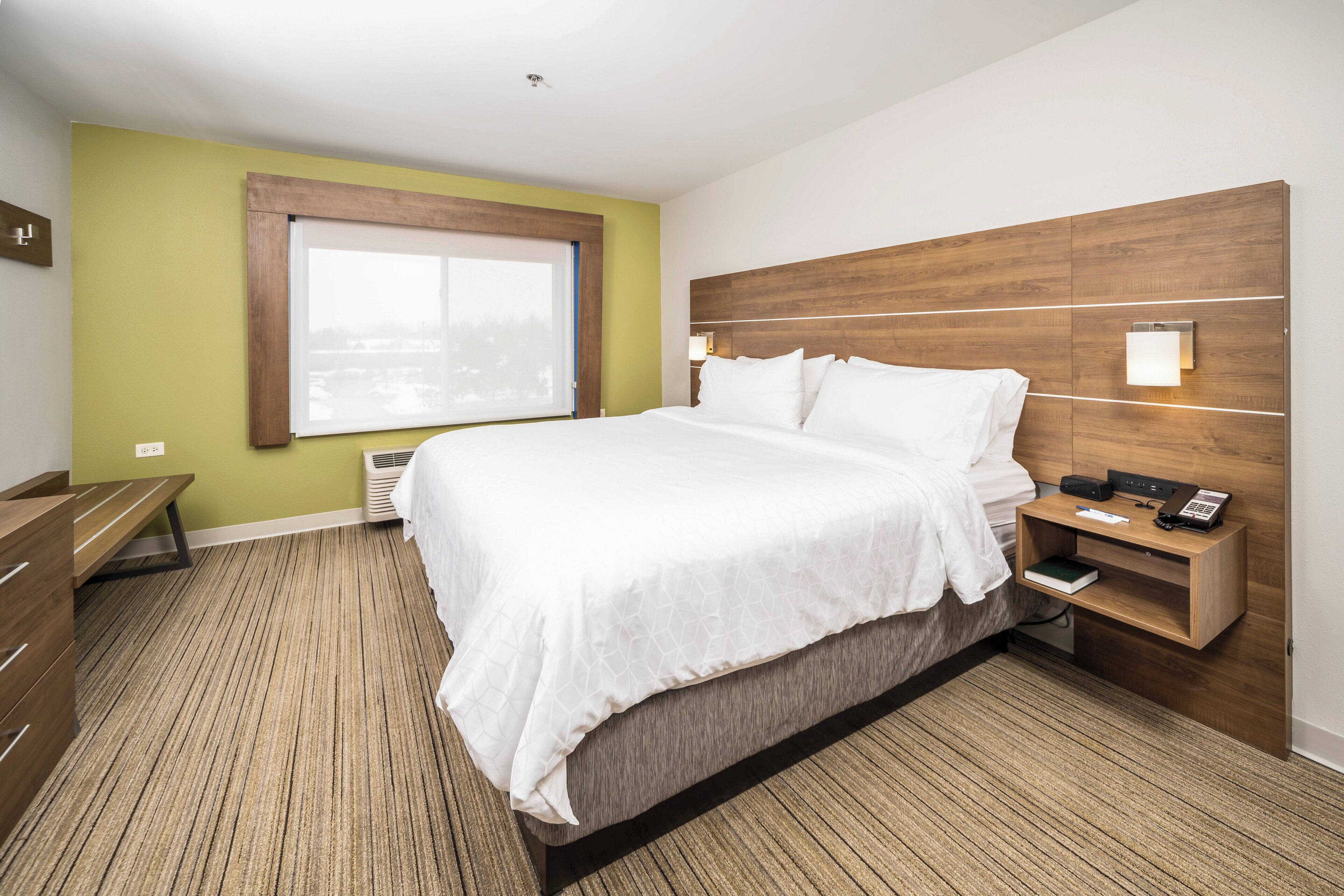 A hotel room with a large bed, bedside table, and a window.