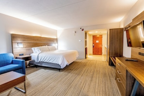 Habitación de hotel con cama, escritorio, silla, televisor y piso de madera.