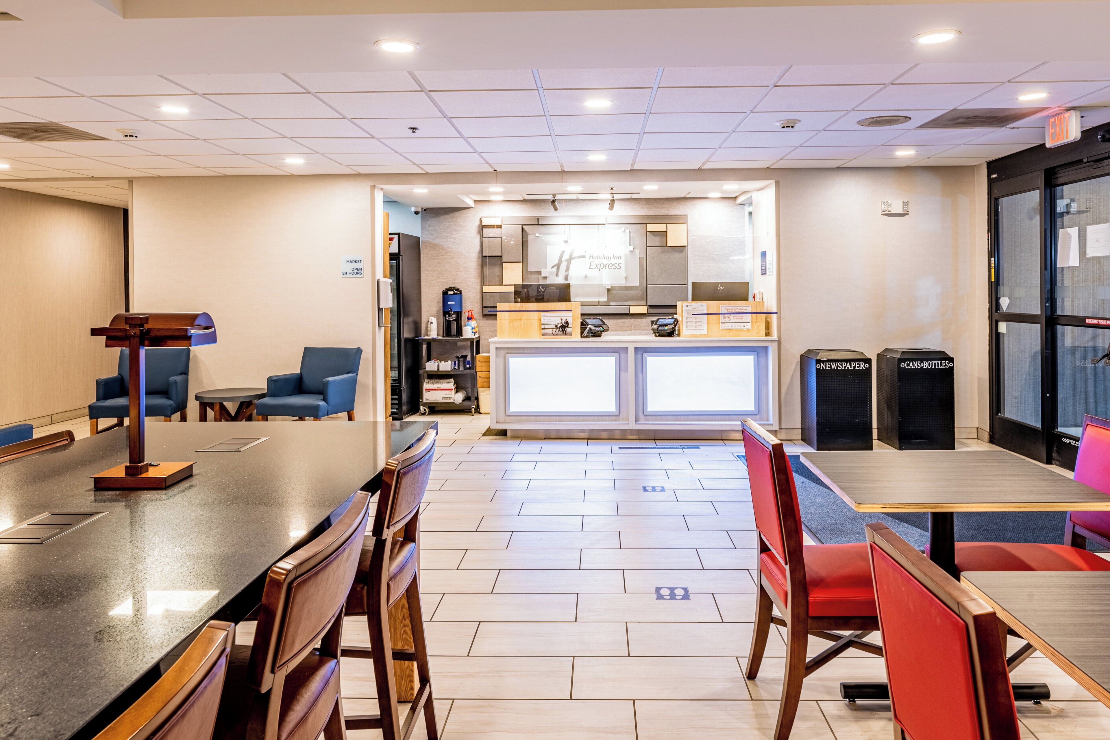 Een hotel lobby met een receptiebalie, een zithoek en een kitchenette op de achtergrond.