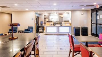 Een hotel lobby met een receptiebalie, een zithoek en een kitchenette op de achtergrond.