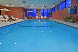 Una piscina interior con sillas de descanso y una mesa, rodeada de ventanas con iluminación azul.