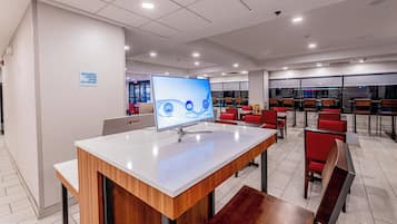 A modern business center with a computer station, seating area, and a sign indicating 24-hour operation.