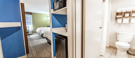 Ein Hotelzimmer mit Bett, Mikrowelle, Minikühlschrank und einem Badezimmer mit Toilette und Handtuchhalter.