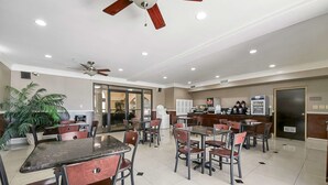 A spacious dining area with multiple tables and chairs, ceiling fans, and a kitchen area in the background.