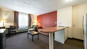 A compact hotel room with a kitchenette, a sofa, a small dining table, and a desk.
