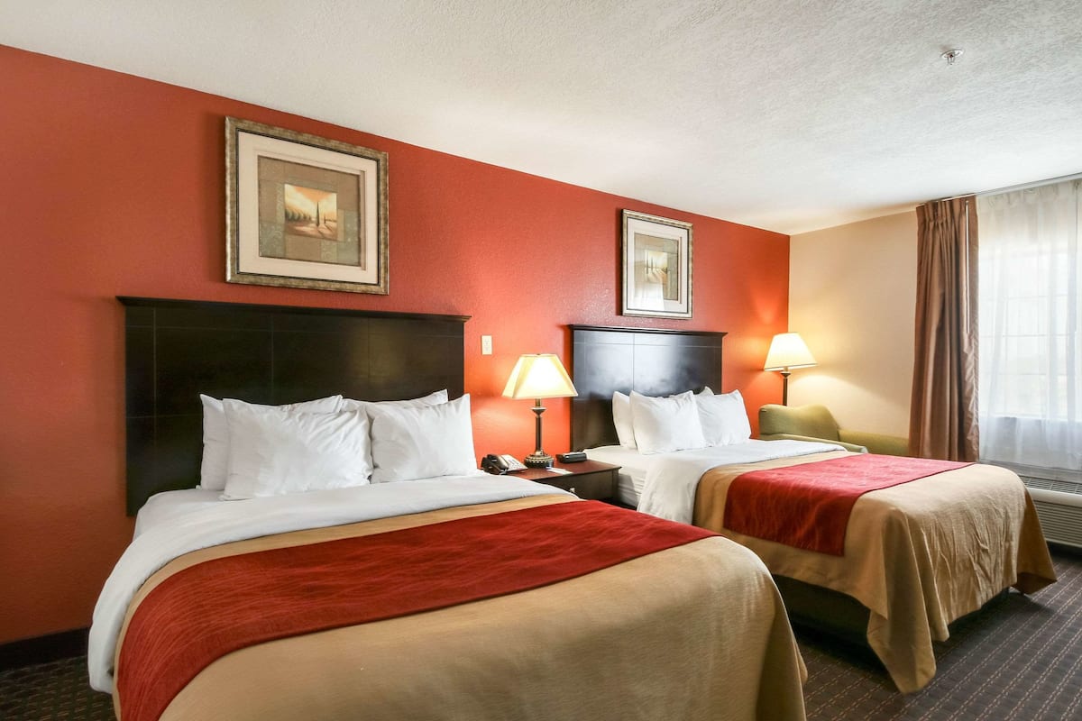 A hotel room with two beds, red walls, and framed pictures above the beds.