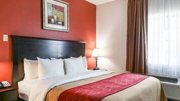 A hotel room with a large bed, a nightstand with a phone, a framed picture on the wall, and a window with curtains.