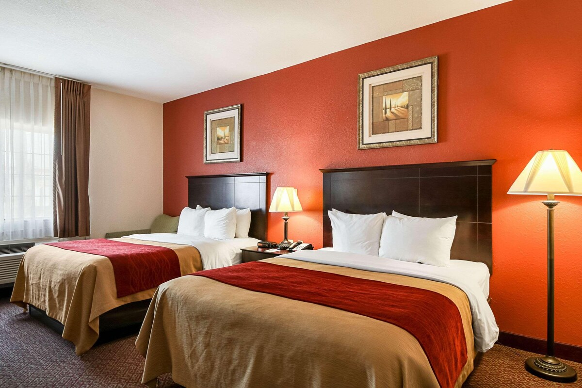 A hotel room with two beds, red walls, framed pictures, and a standing lamp.