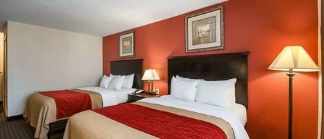 A hotel room with two beds, red walls, and a lamp.