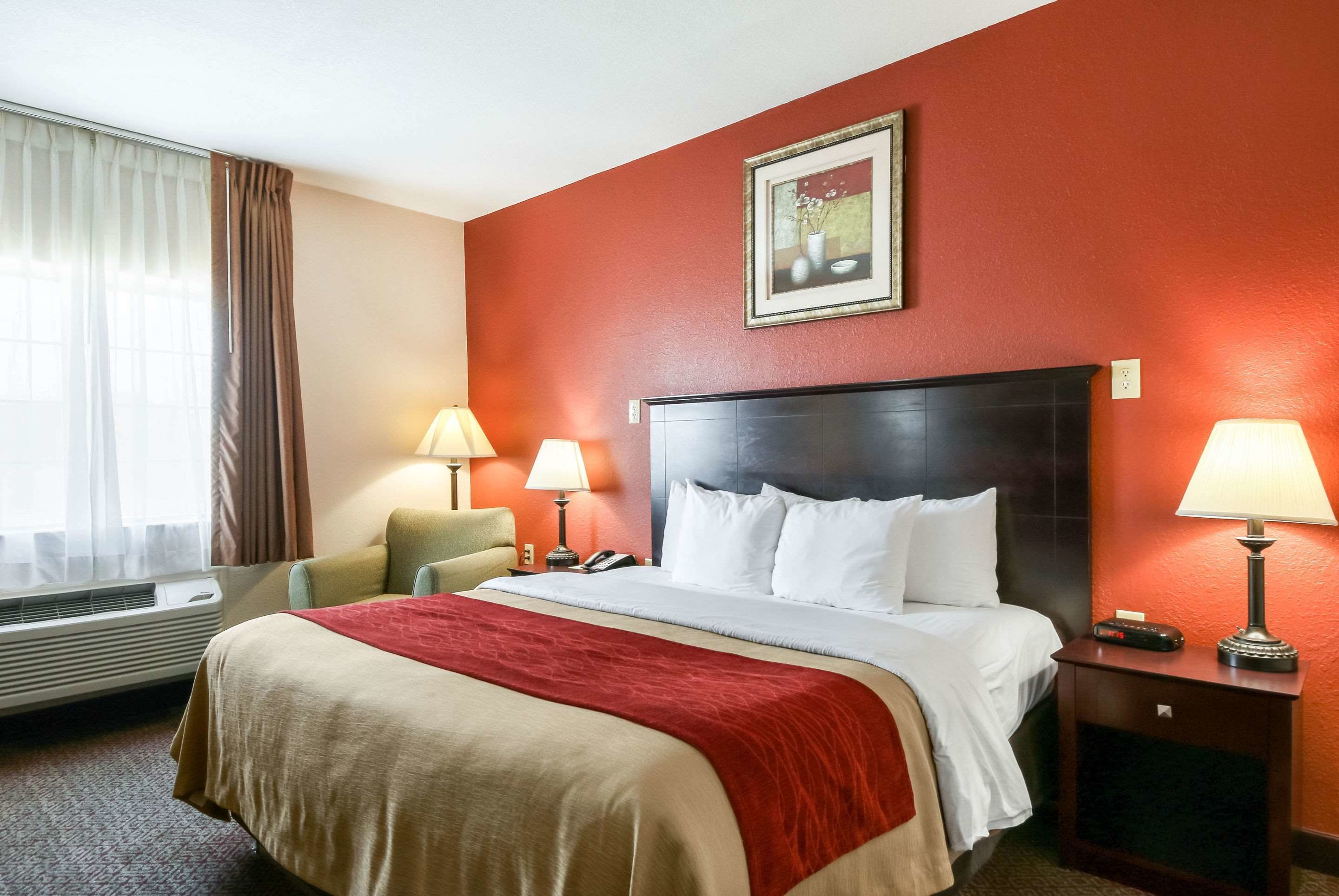 Camera d'albergo con un letto grande, due abat-jour, una sedia, un comodino e un quadro appeso al muro.