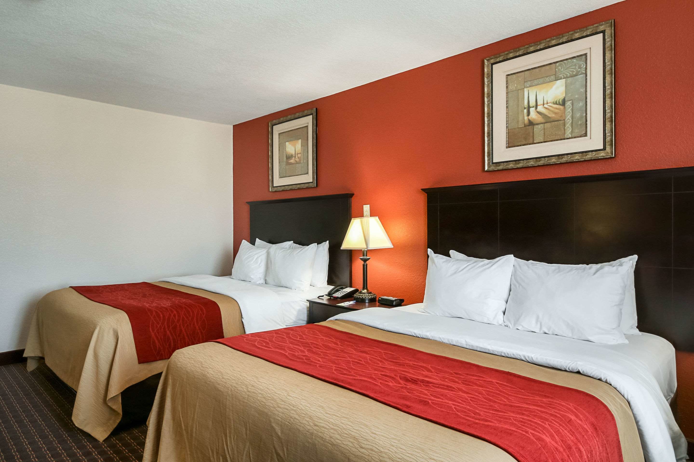 A hotel room with two beds, a nightstand with a lamp, and two framed pictures on the wall.