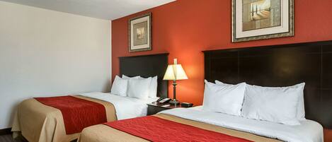 A hotel room with two beds, a nightstand with a lamp, and two framed pictures on the wall.