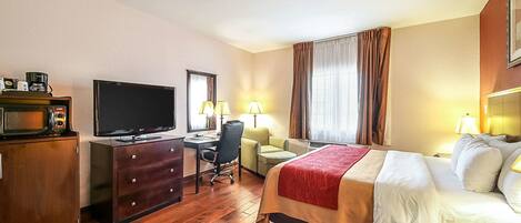 Una habitación de hotel con cama, escritorio, televisión y un armario de madera.