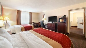A hotel room with two beds, a desk, a television, and a kitchenette.