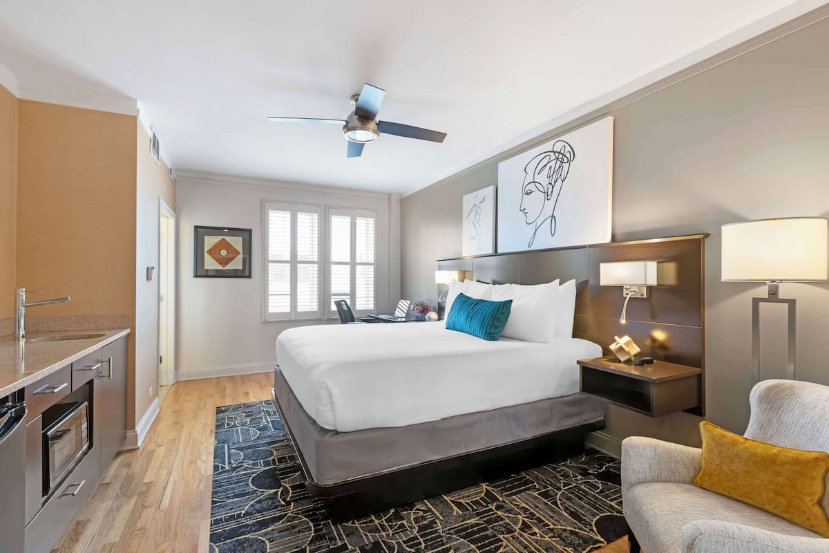 A hotel room with a bed, a desk, a chair, a ceiling fan, and artwork on the walls.