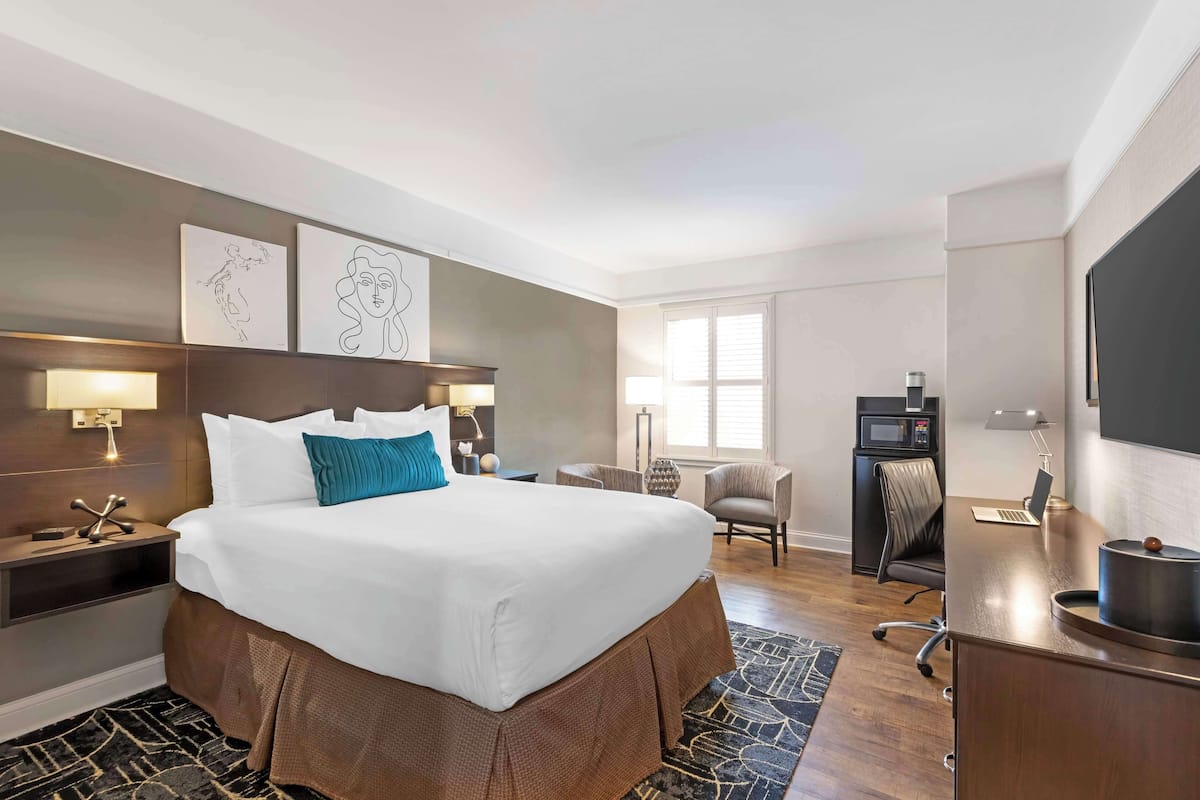 A hotel room with a large bed, a desk with a laptop, a TV, a microwave, and a chair.