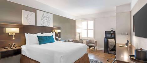 A hotel room with a large bed, a desk with a laptop, a TV, a microwave, and a chair.
