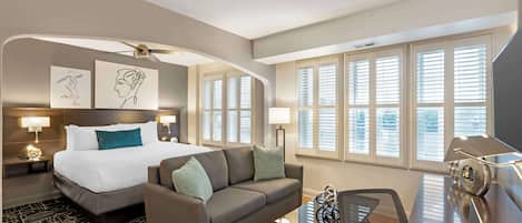 Une chambre d’hôtel moderne équipée d’un lit, d’un canapé, d’un bureau avec un ordinateur portable et de grandes fenêtres avec des stores.