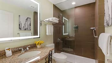 A modern bathroom with a granite sink, a large mirror, a glass shower enclosure, and a white toilet.
