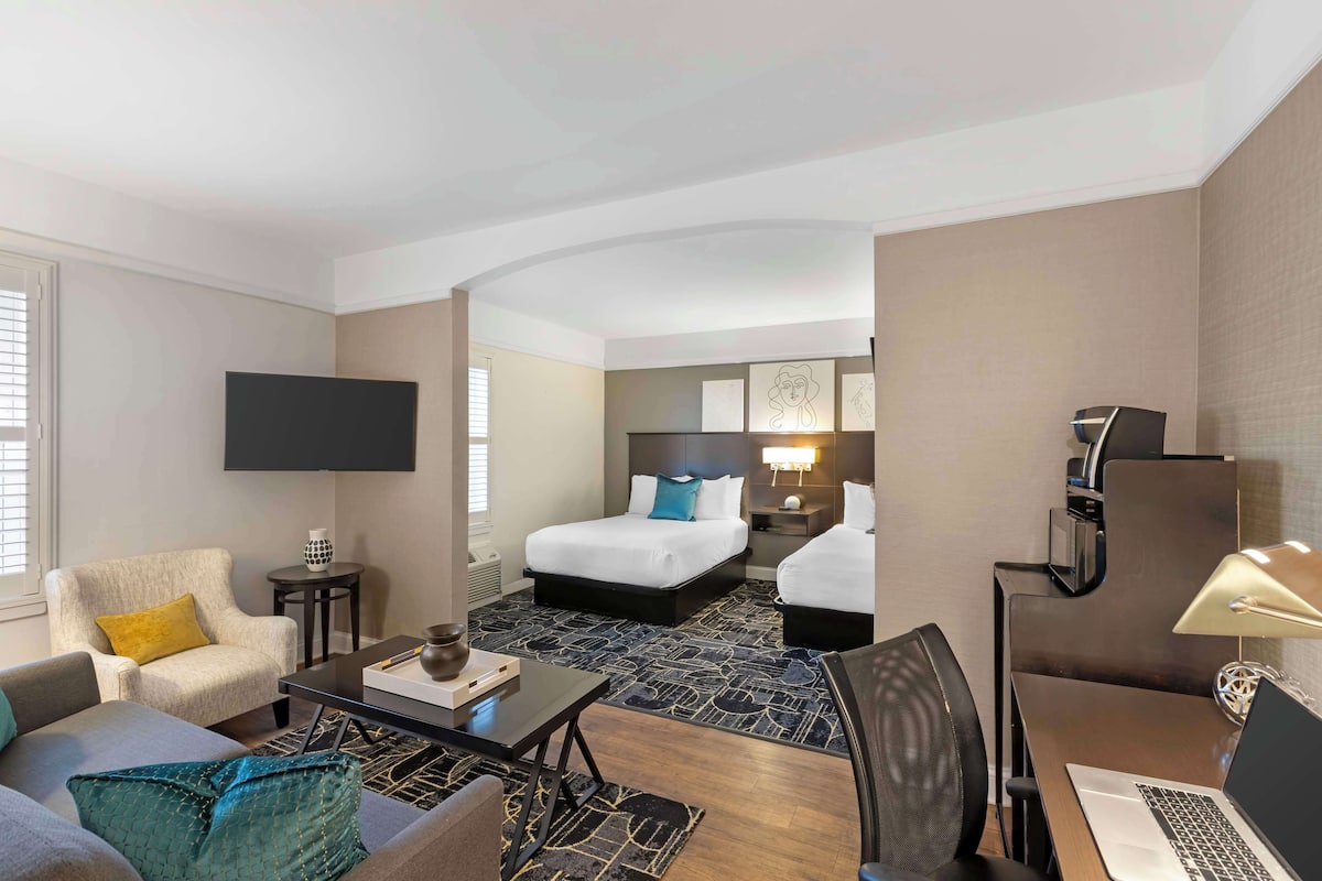 A hotel room with a bed, a sofa, a desk, a TV, and a lamp.