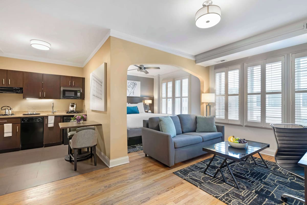 A modern apartment with a kitchen, dining area, and living room. It features a sofa, a dining table, and a kitchen with a microwave and cabinets.