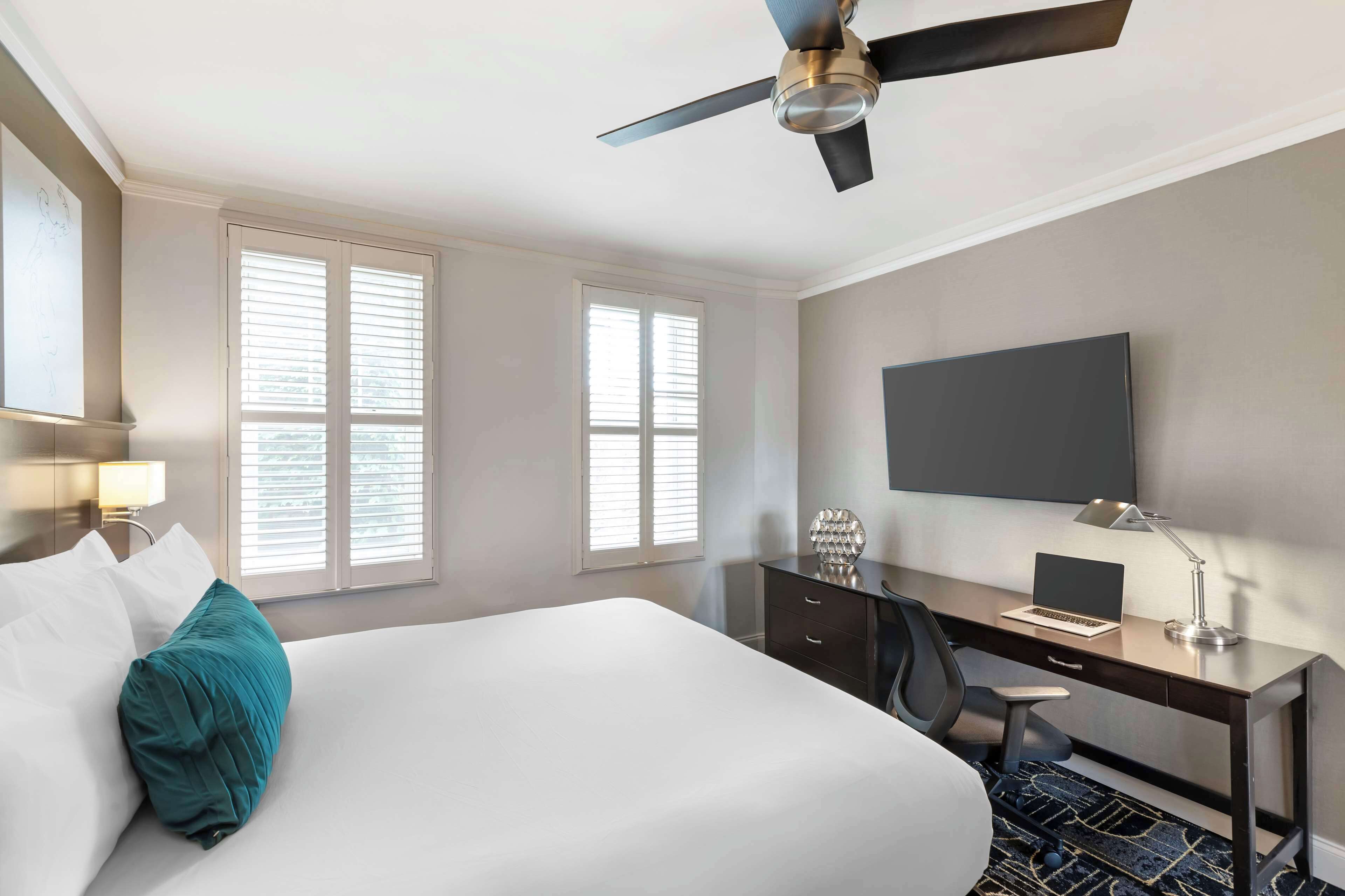 Habitación de hotel con cama, escritorio, silla y ventilador de techo.