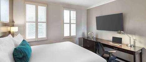 Habitación de hotel con cama, escritorio, silla y ventilador de techo.