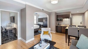 A modern hotel room with a desk, chair, and a dining area with a table and chairs.