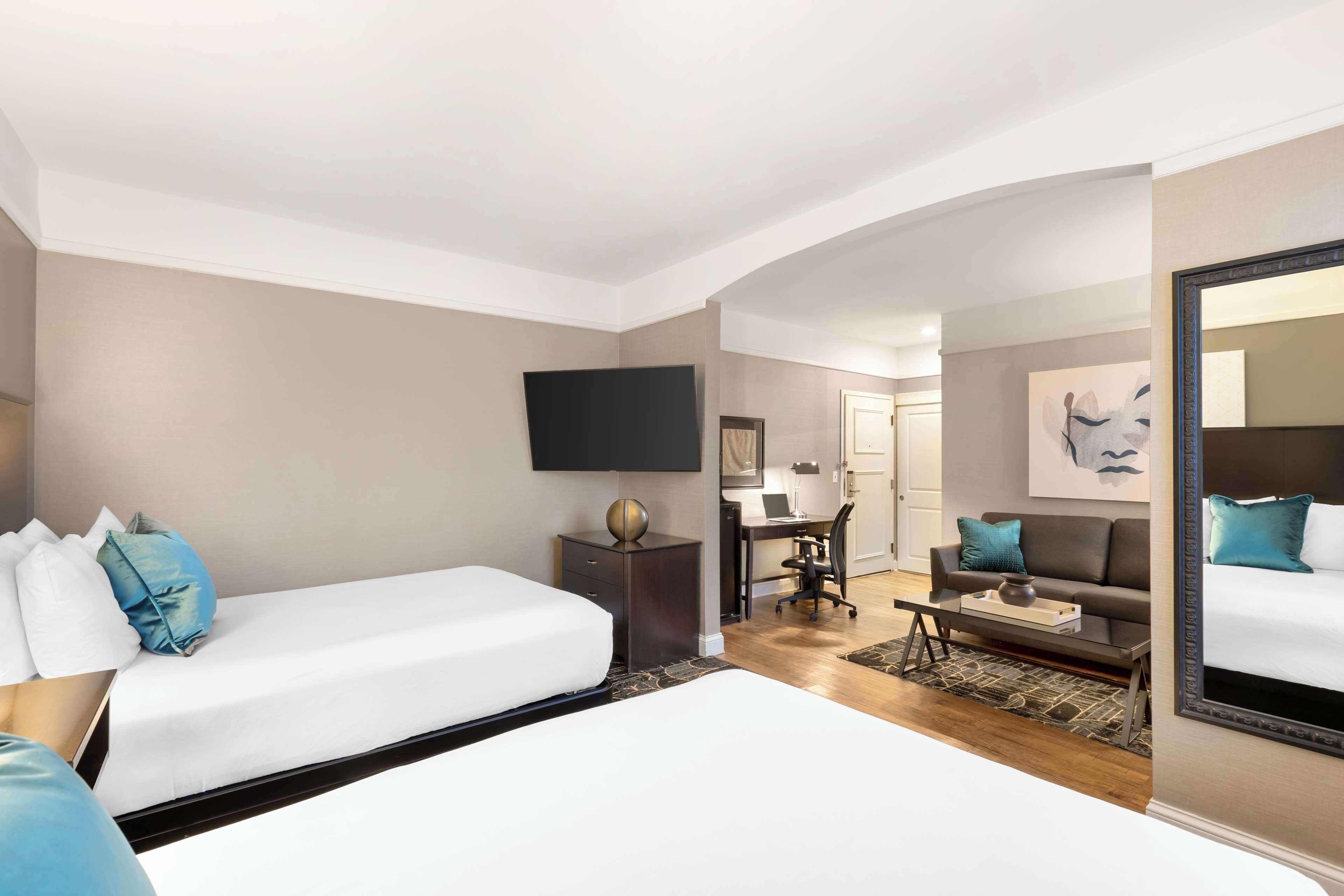 A hotel room with two beds, a desk, a chair, a coffee table, and a TV.