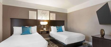A hotel room with two beds, a nightstand, a lamp, and artwork on the wall.