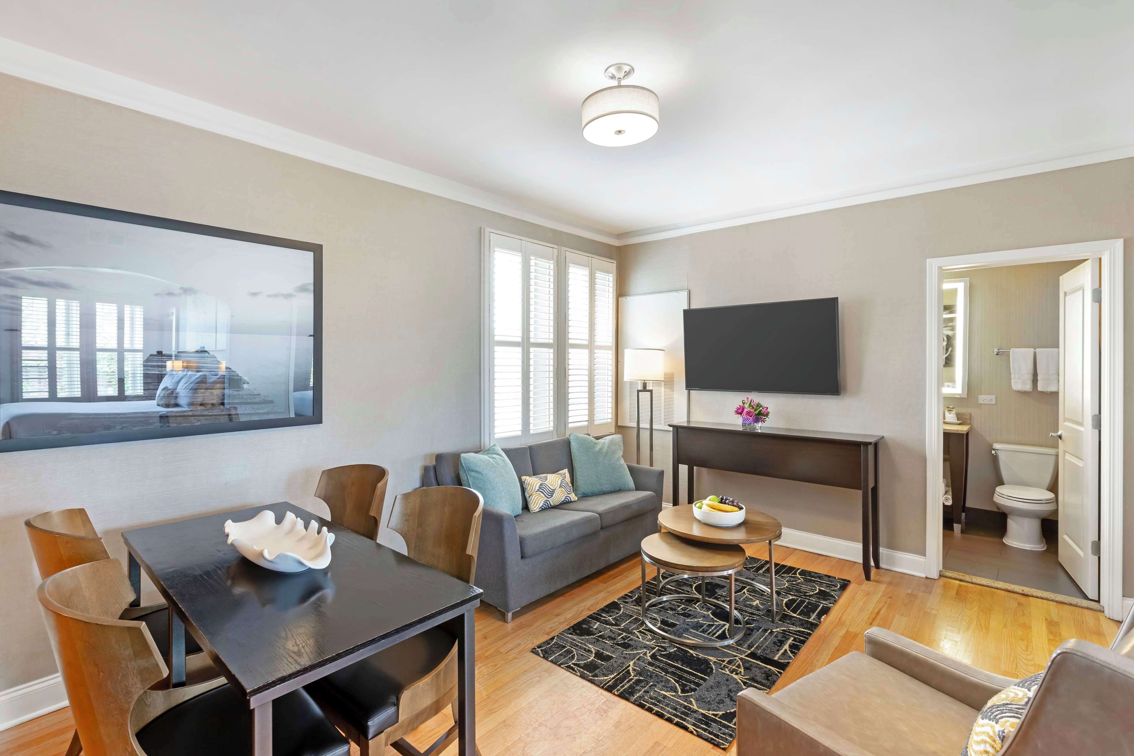 A modern living room with a sofa, dining table, and chairs, a flat-screen TV, and a view of the outside.