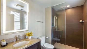 A modern bathroom with a large mirror, granite countertop, white toilet, and a glass-enclosed shower area.