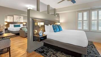 Quarto de hotel moderno com uma cama grande, uma escrivaninha, uma cadeira, uma mesa de cabeceira e um ventilador de teto.