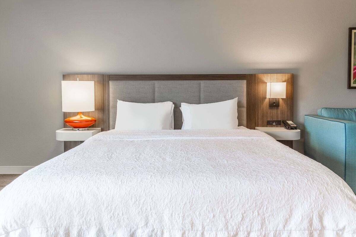 Una habitación de hotel con una cama grande, dos mesitas de noche con lámparas, un teléfono y una silla azul.